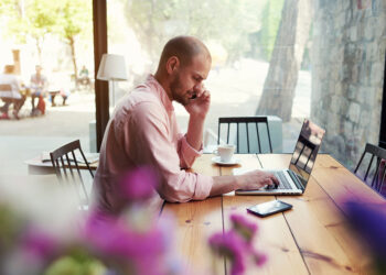 Young male student work on computer touchpad, freelancer working on notebook at hipster loft space